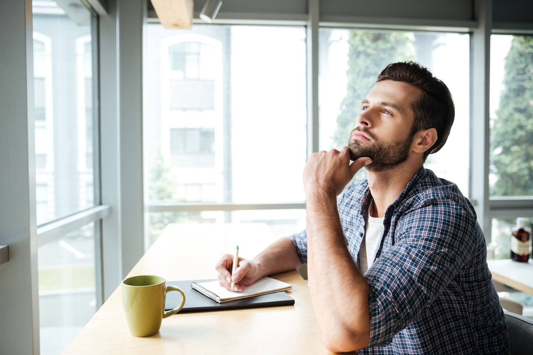 a man is sitting at a table with a notebook and a cup of coffee while thinking intensely